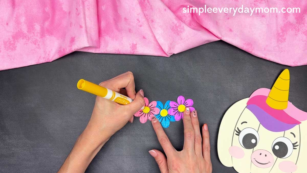 Hands adding details to the colorful flowers for the unicorn pumpkin craft.