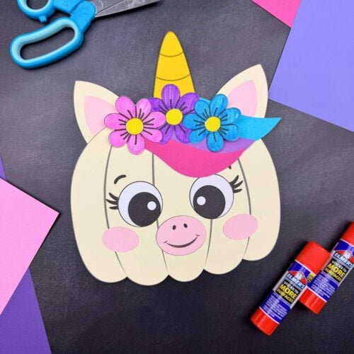 A completed craft featuring a unicorn pumpkin with a horn, ears, colorful mane, and flowers alongside craft supplies.