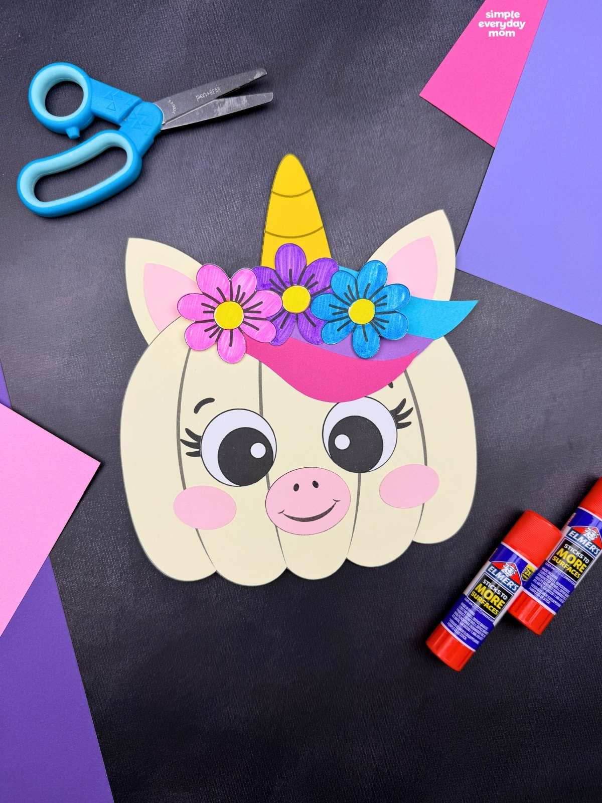 A completed craft featuring a unicorn pumpkin with a horn, ears, colorful mane, and flowers alongside craft supplies.