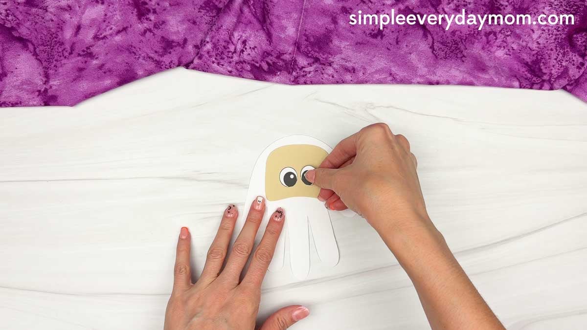 Hands gluing the eyes onto the face of the Wizard Handprint Craft.