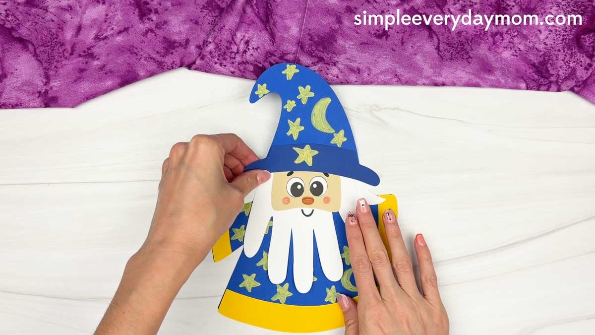 Hands placing the wizard head onto the decorated robe for the Wizard Handprint Craft.