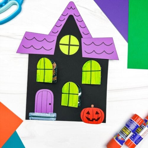 A completed craft featuring a Peekaboo Haunted House with opening windows, a colorful roof, door, and jack-o'-lantern.
