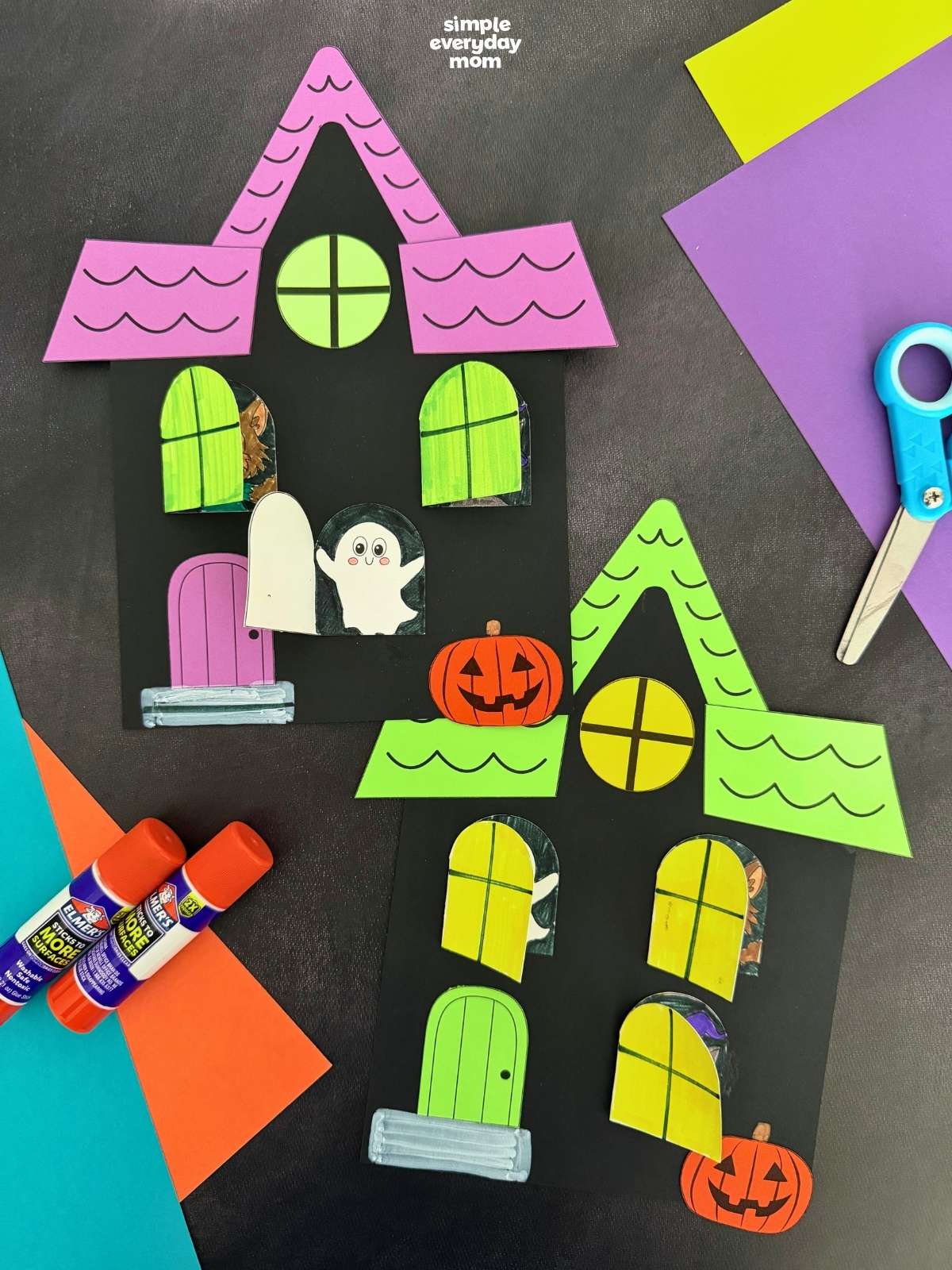 A completed craft display featuring two Peekaboo Haunted House Crafts with opening windows, Halloween characters, pumpkins, and craft supplies.