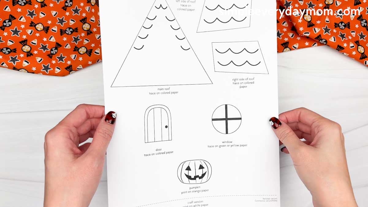 Hands holding the Peekaboo Haunted House Craft printable template featuring roof, door, window, and pumpkin pieces.