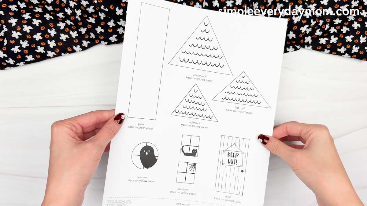 Hands holding a haunted house shape craft template featuring roof, window, door, and grass pieces.