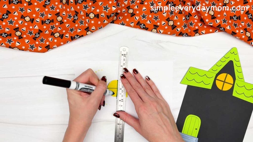 Hands using a ruler and marker to draw window lines on a piece for the Peekaboo Haunted House Craft.