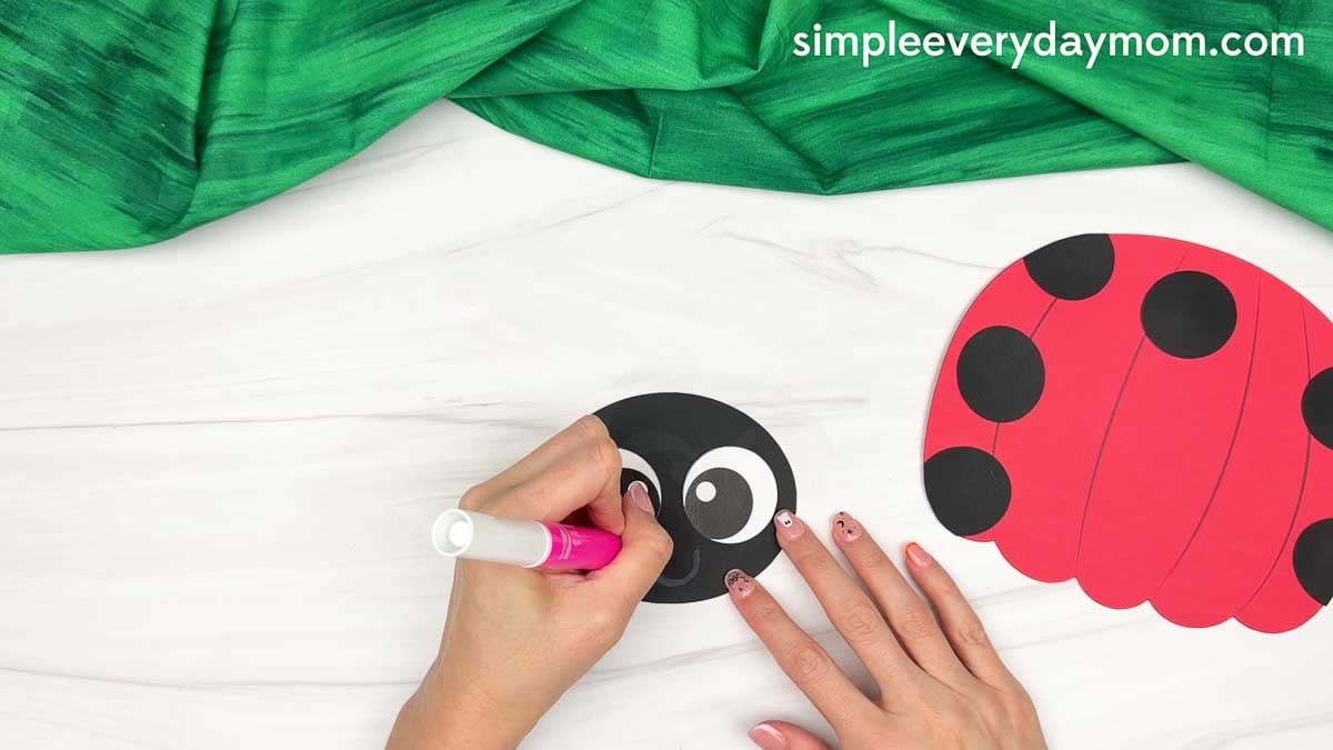 Hands drawing a smile on the ladybug head beside the spotted pumpkin body.