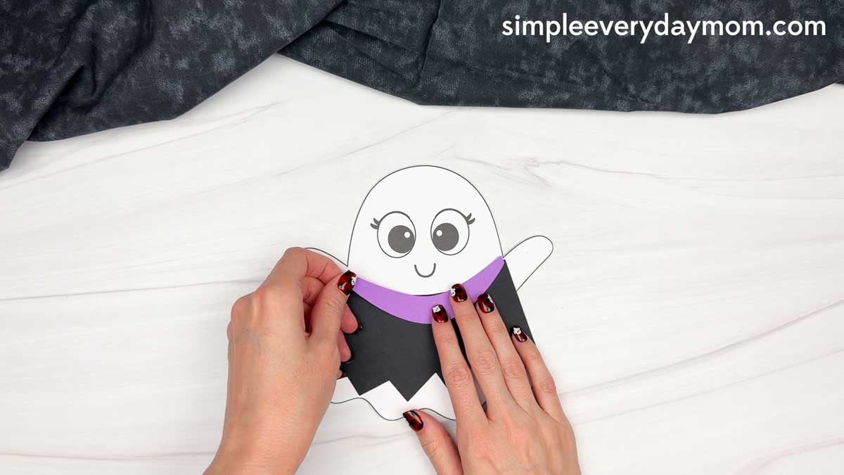 Hands attaching the witch dress collar across the top of the ghost’s dress.