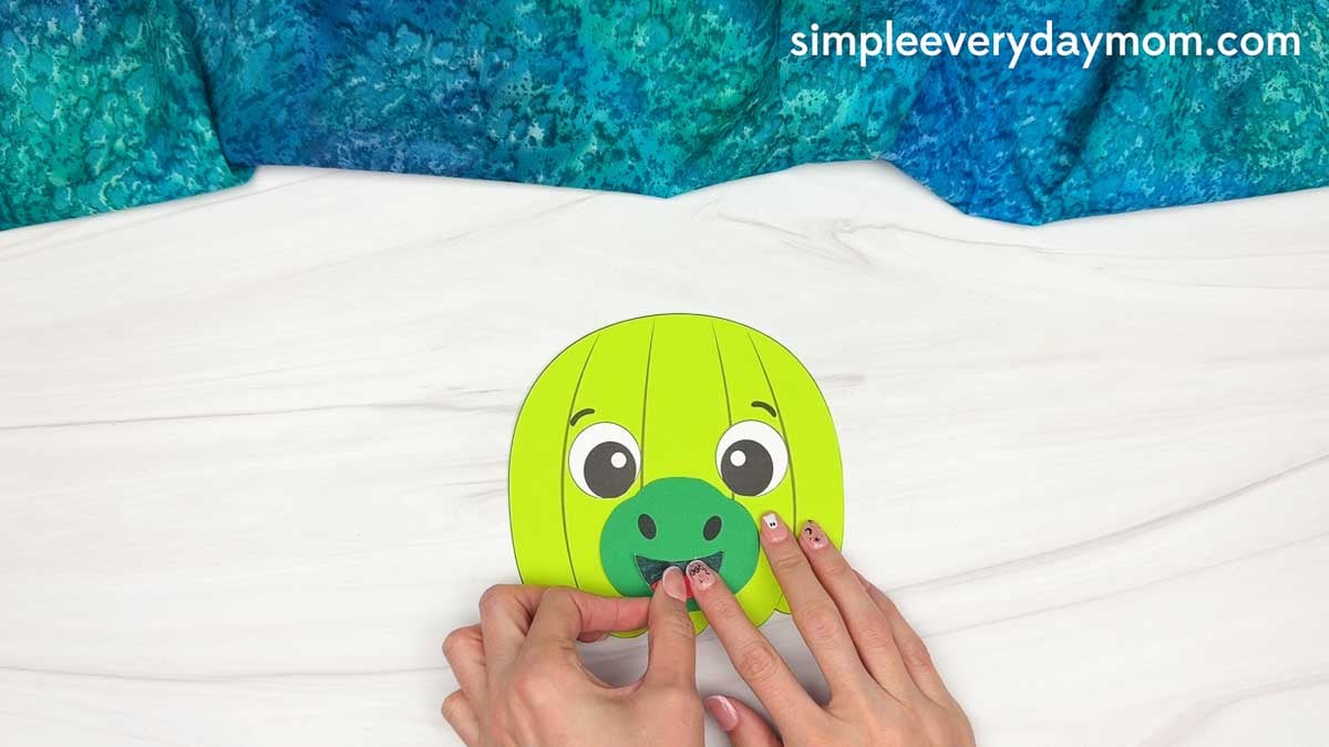 Hands gluing the mouth onto the snout of the dinosaur pumpkin craft.