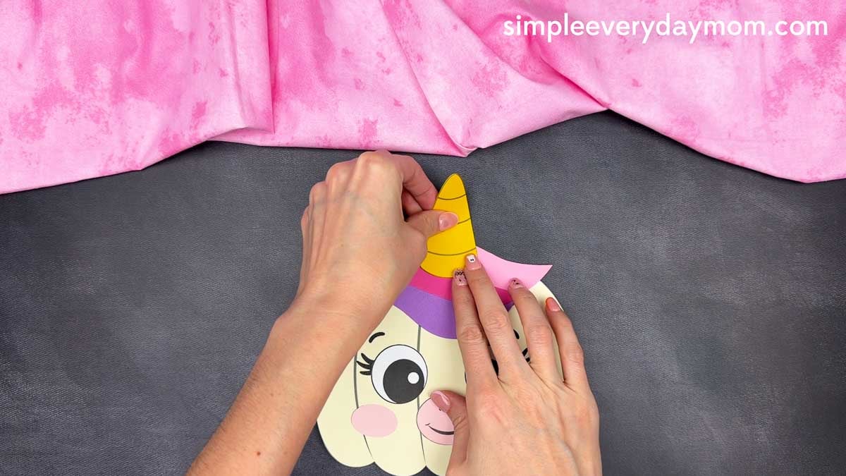 Hands gluing the horn onto the top center of the unicorn pumpkin craft.