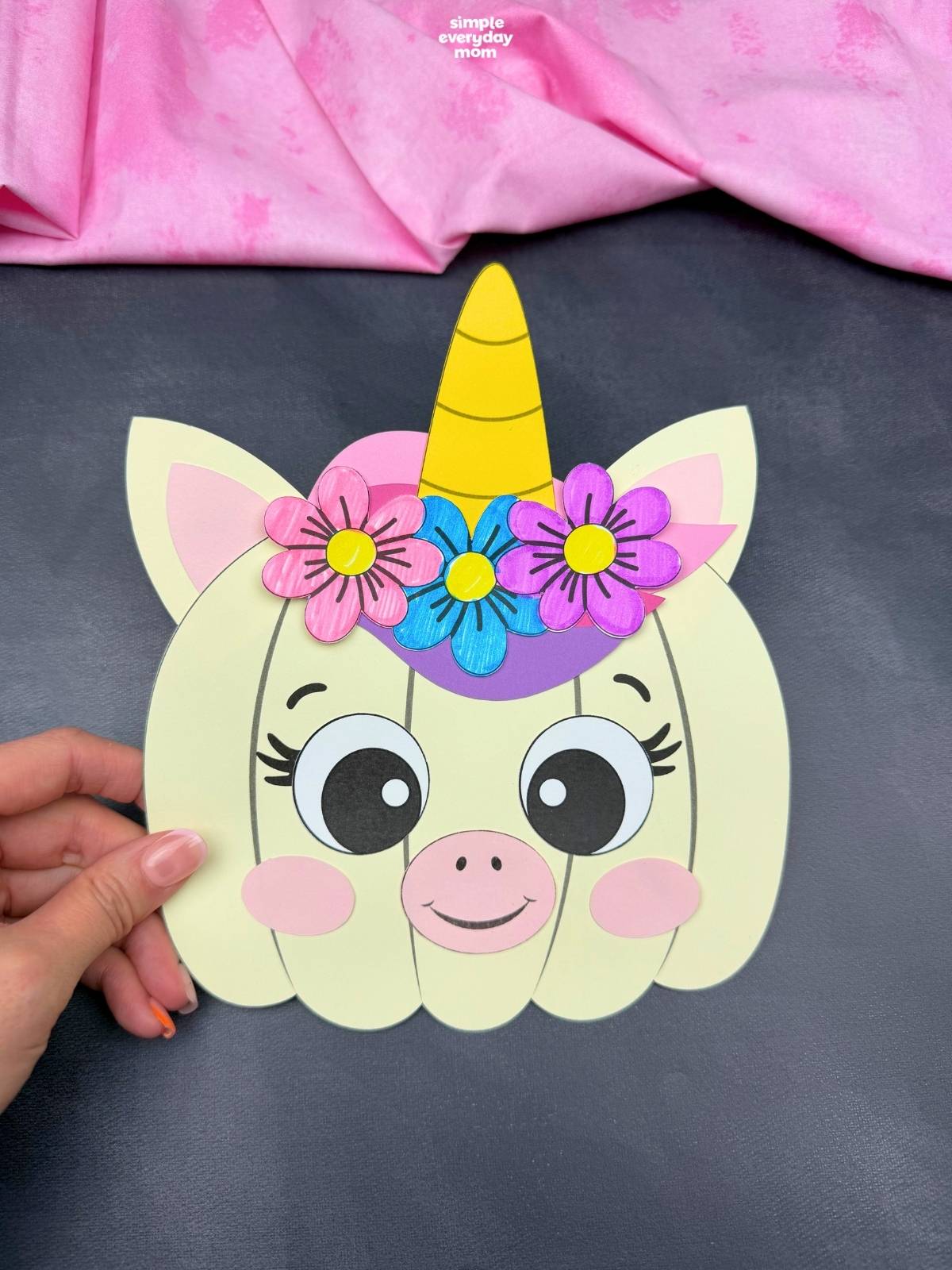 A completed craft featuring a unicorn pumpkin with a horn, ears, colorful flowers, and a smiling face.