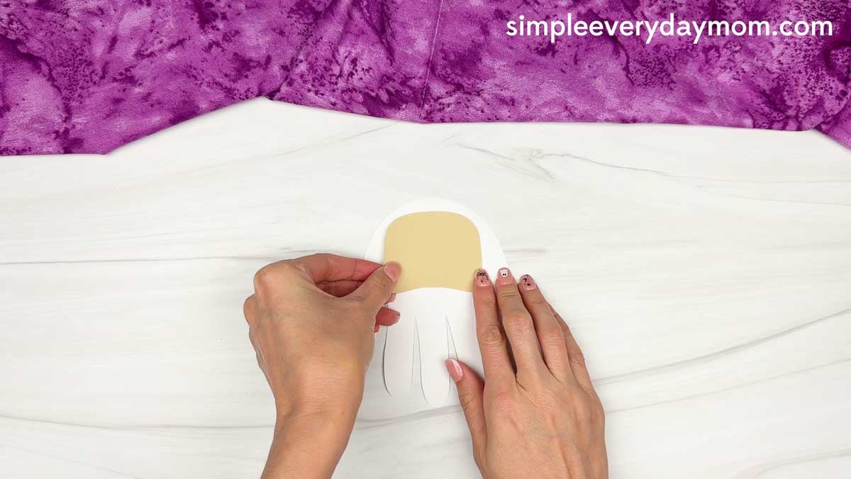 Hands placing the face piece onto the palm area of the Wizard Handprint Craft.