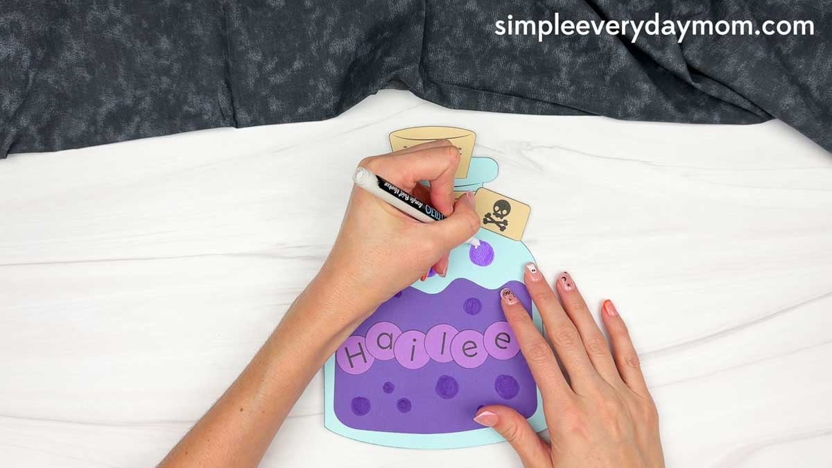 Hands using a marker to add bubbles around the name on the Halloween potion bottle craft.