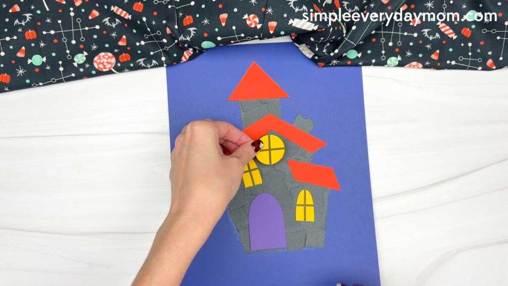 Hands placing a round yellow window onto the upper section of the torn paper haunted house.