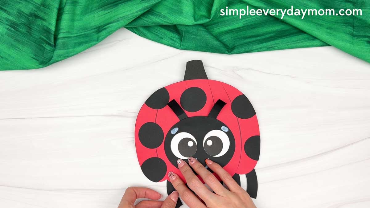 Hands gluing the ladybug legs to the bottom of the pumpkin body.