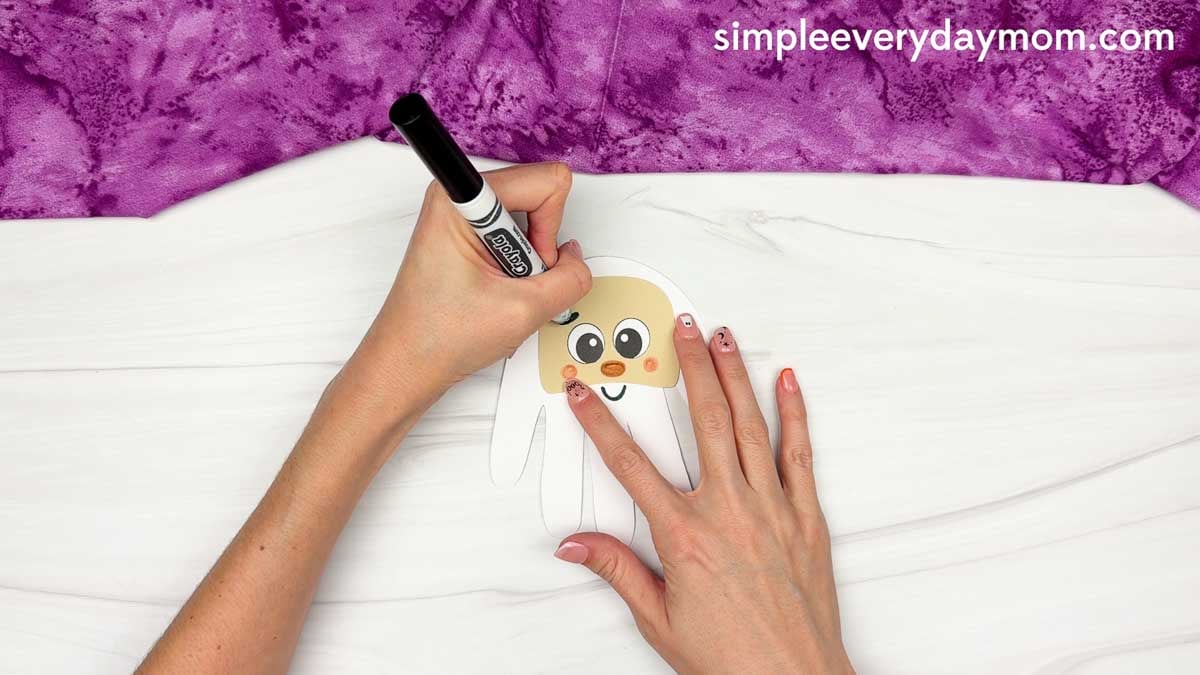 Hands drawing eyebrows above the eyes of the Wizard Handprint Craft with a black marker.