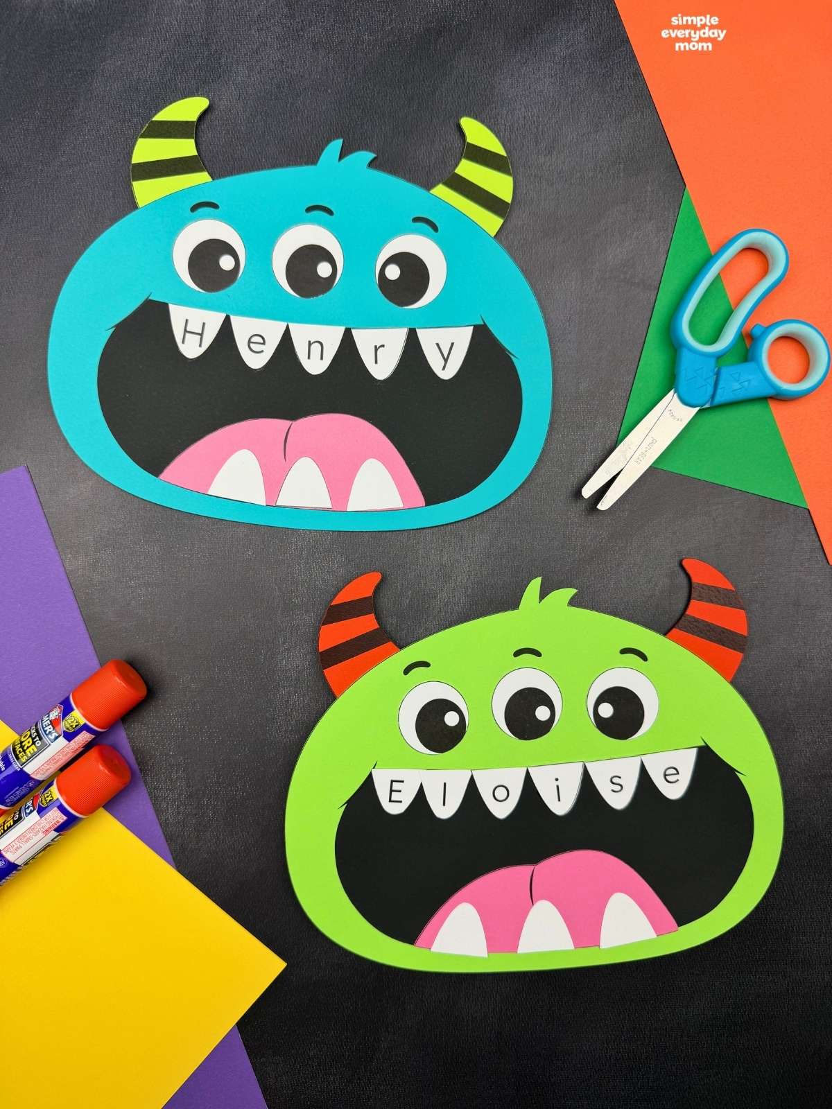 Side by side completed monster name crafts with three eyes, striped horns, and names written across their teeth.