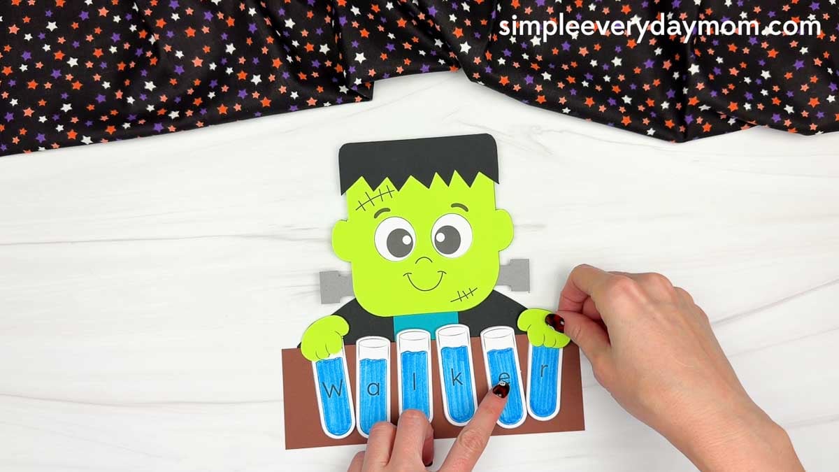 Hands gluing the Frankenstein hands above the lettered test tubes spelling the child’s name.
