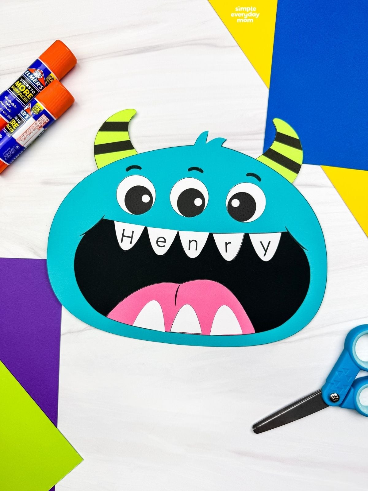 A completed craft featuring a blue monster with three eyes, striped horns, and the name Henry written across its teeth.