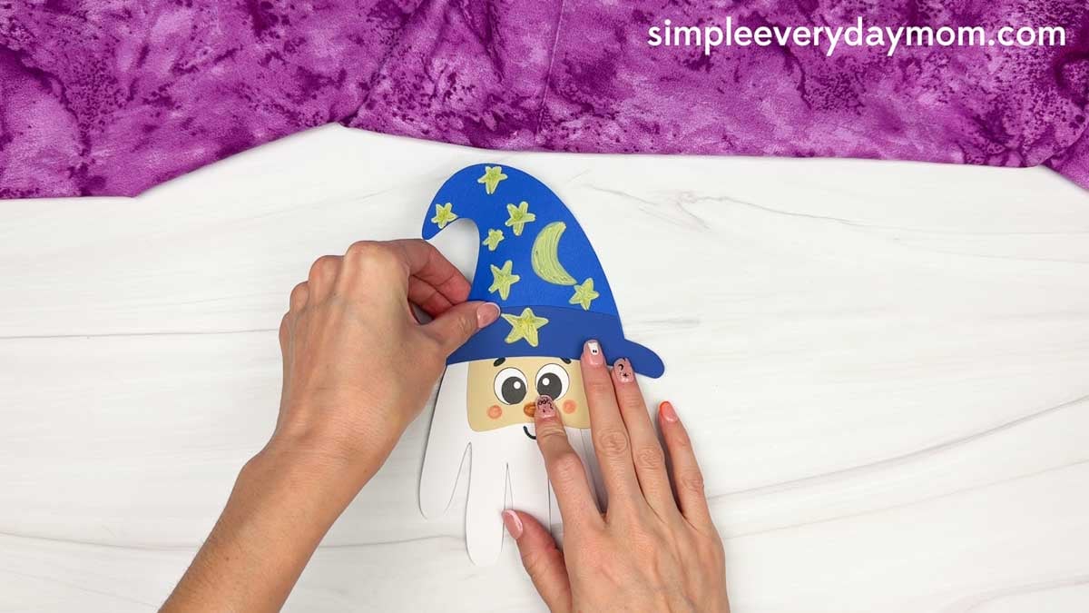Hands placing the decorated hat onto the top of the Wizard Handprint Craft.