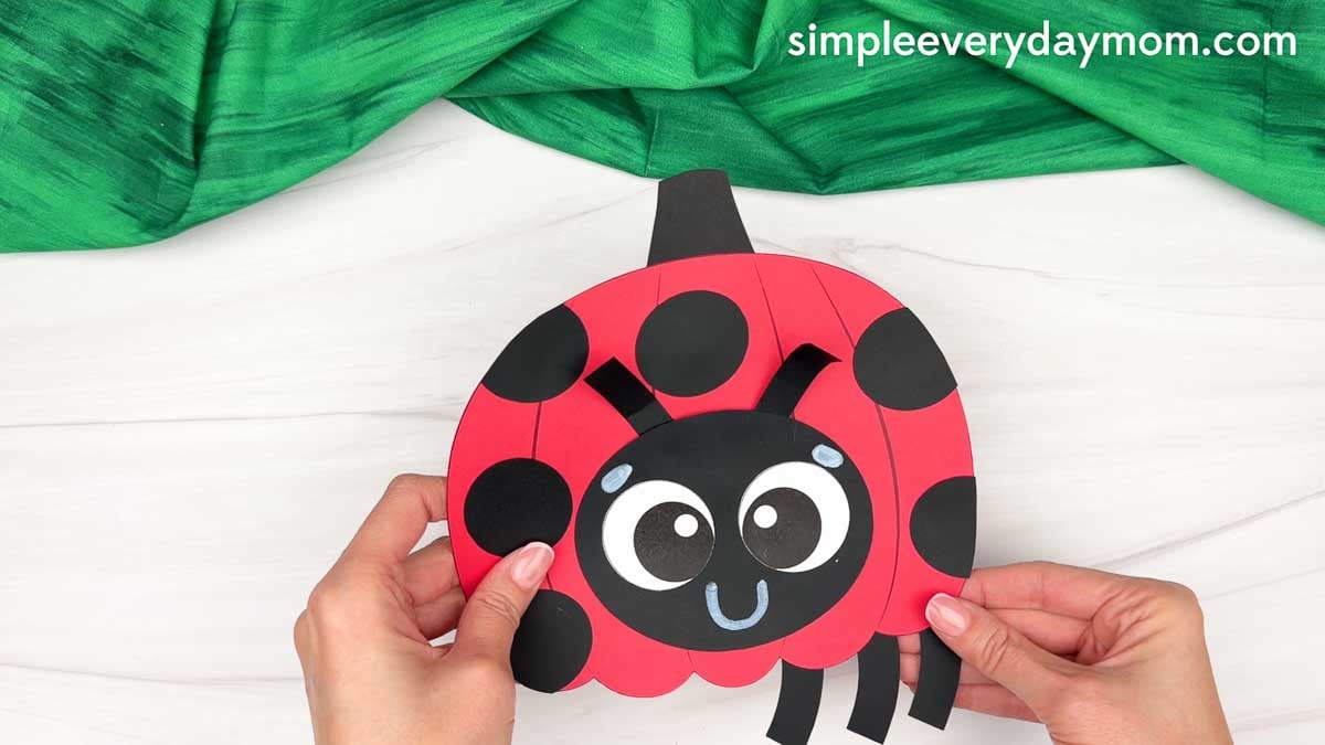 Hands attaching the ladybug legs to the bottom of the pumpkin body.