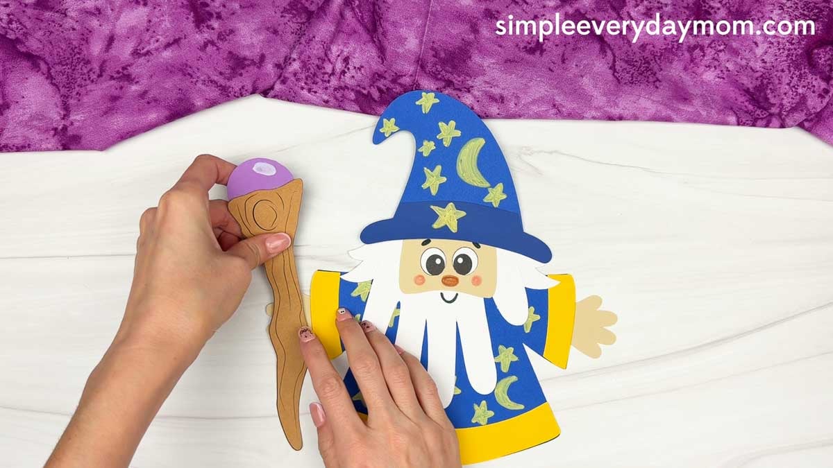 Hands positioning the wizard staff beside the Wizard Handprint Craft.