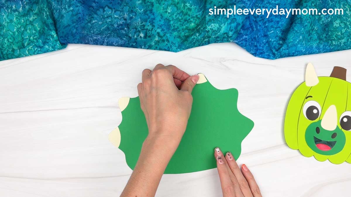 Hands gluing spikes around the edge of the dinosaur frill for the pumpkin craft.