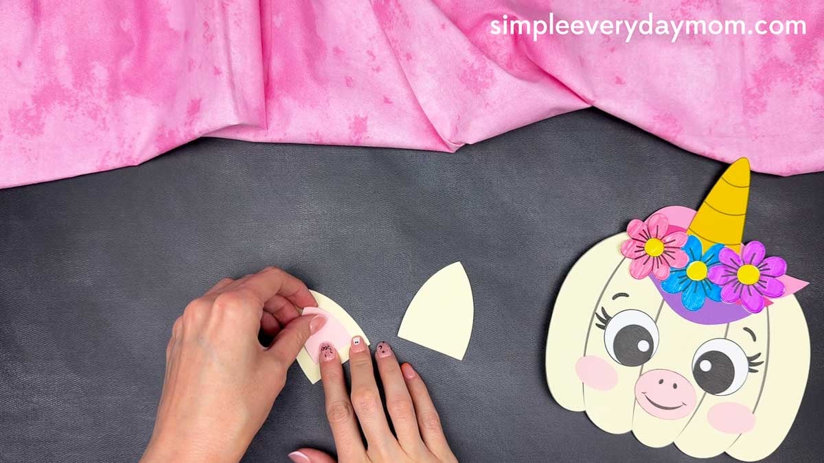 Hands gluing the inner ear piece onto the unicorn ear for the pumpkin craft.