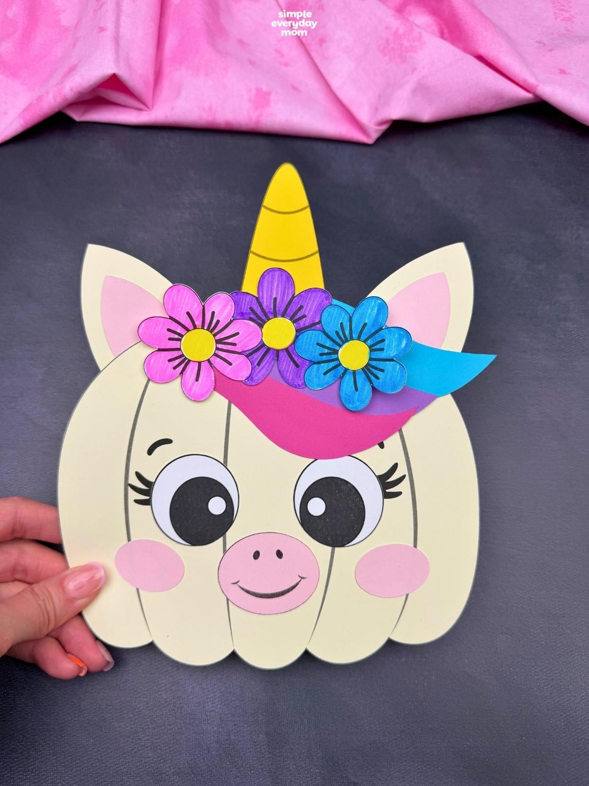 A completed craft featuring a unicorn pumpkin with a horn, ears, colorful mane, flowers, and a smiling face.