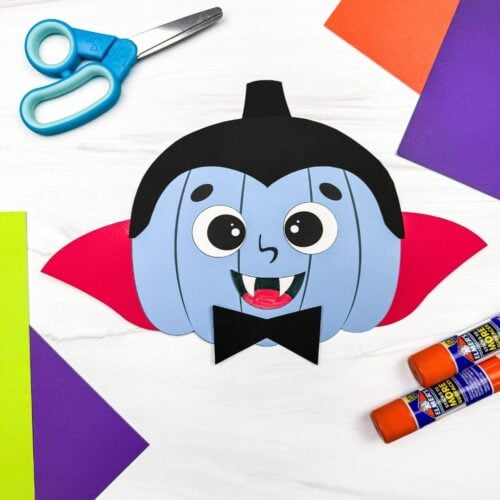 A completed craft showing a vampire pumpkin disguise with a cape, fangs, and bow tie surrounded by craft supplies.