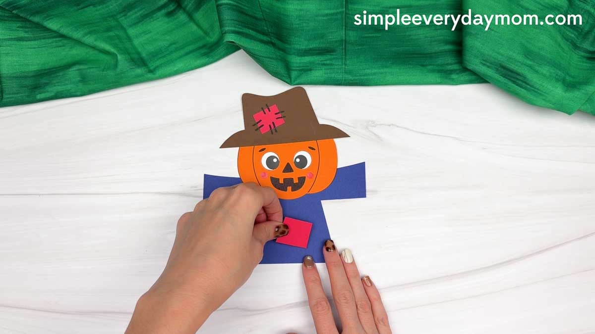 Hands attaching a patch to the center of the scarecrow’s shirt.