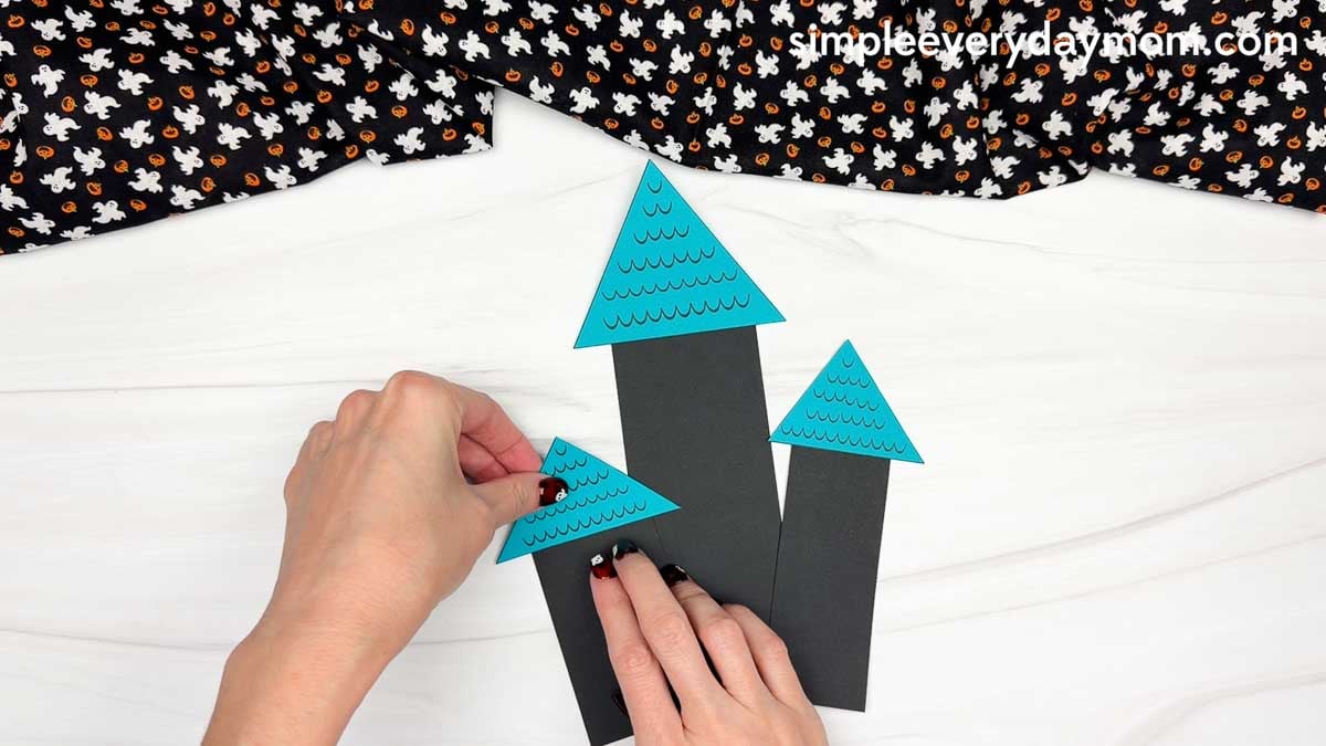 Hands gluing a triangular roof onto the left side of the haunted house shape craft.