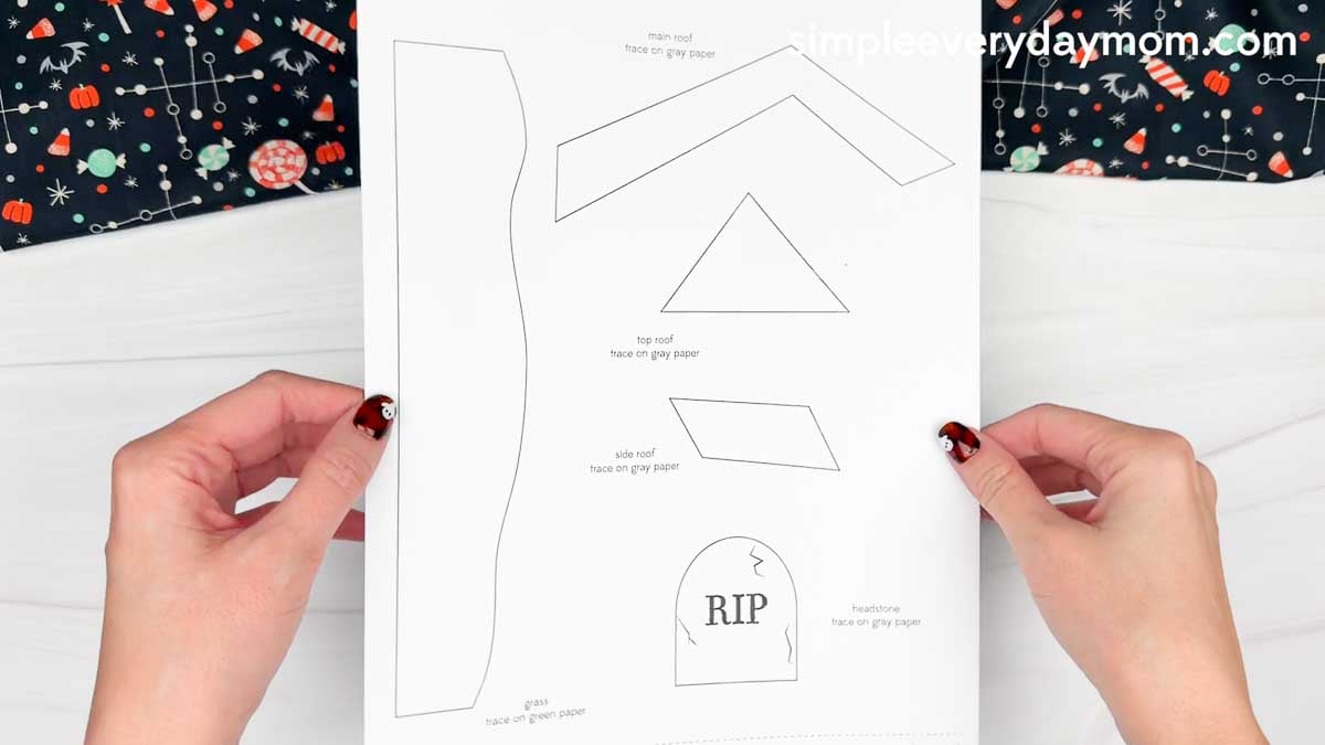 Hands holding the Haunted House Torn Paper Craft printable template showing the roof, grass, and headstone pieces.