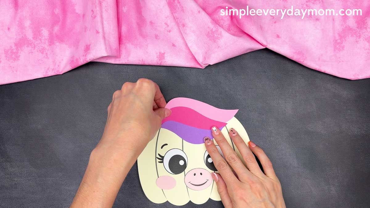 Hands gluing the layered mane onto the top of the unicorn pumpkin craft.