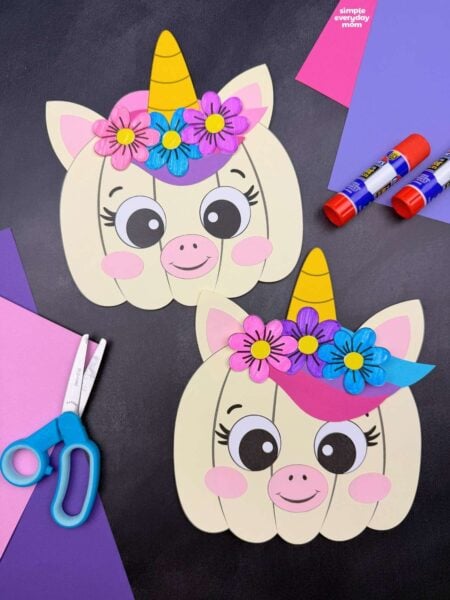 A completed craft showing two unicorn pumpkins with horns, ears, colorful flowers, and smiling faces alongside craft supplies.
