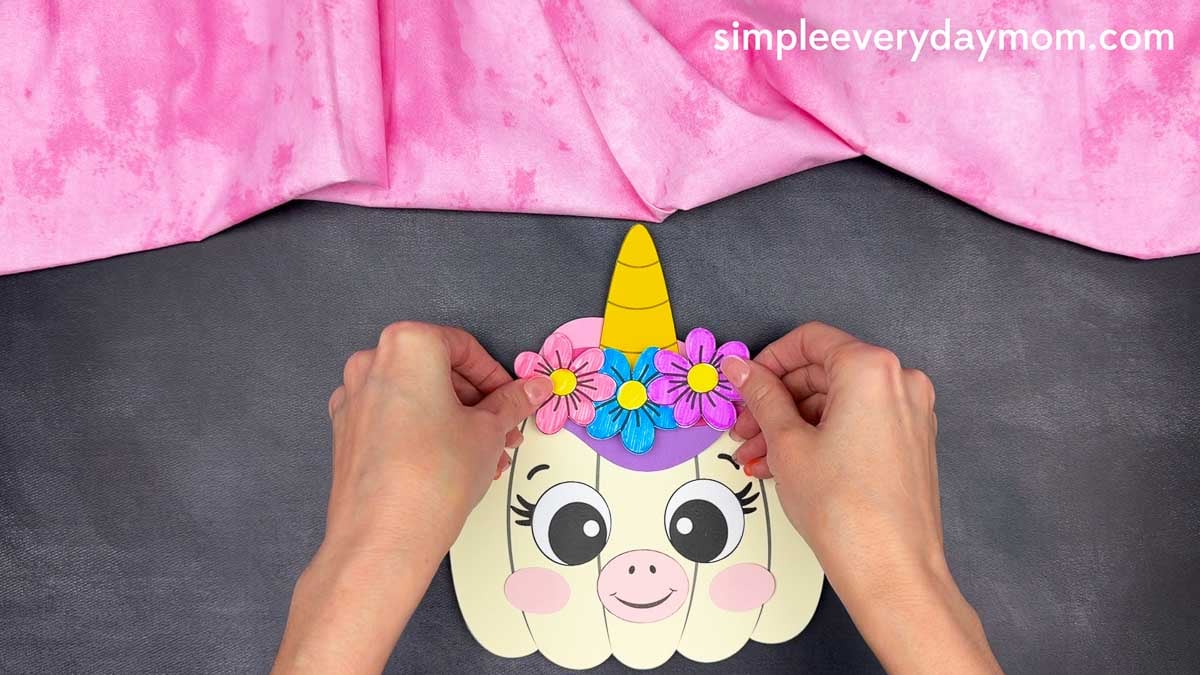 Hands placing colorful flowers across the mane of the unicorn pumpkin craft.