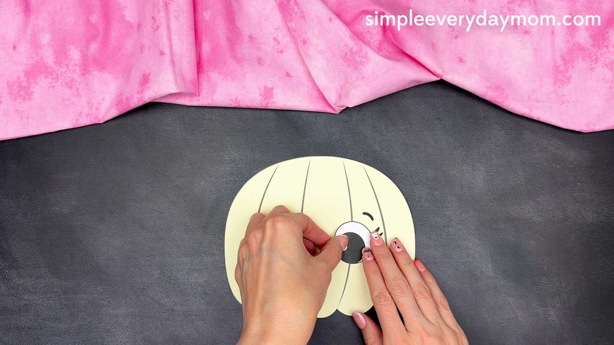 Hands gluing an eye onto the unicorn pumpkin craft.
