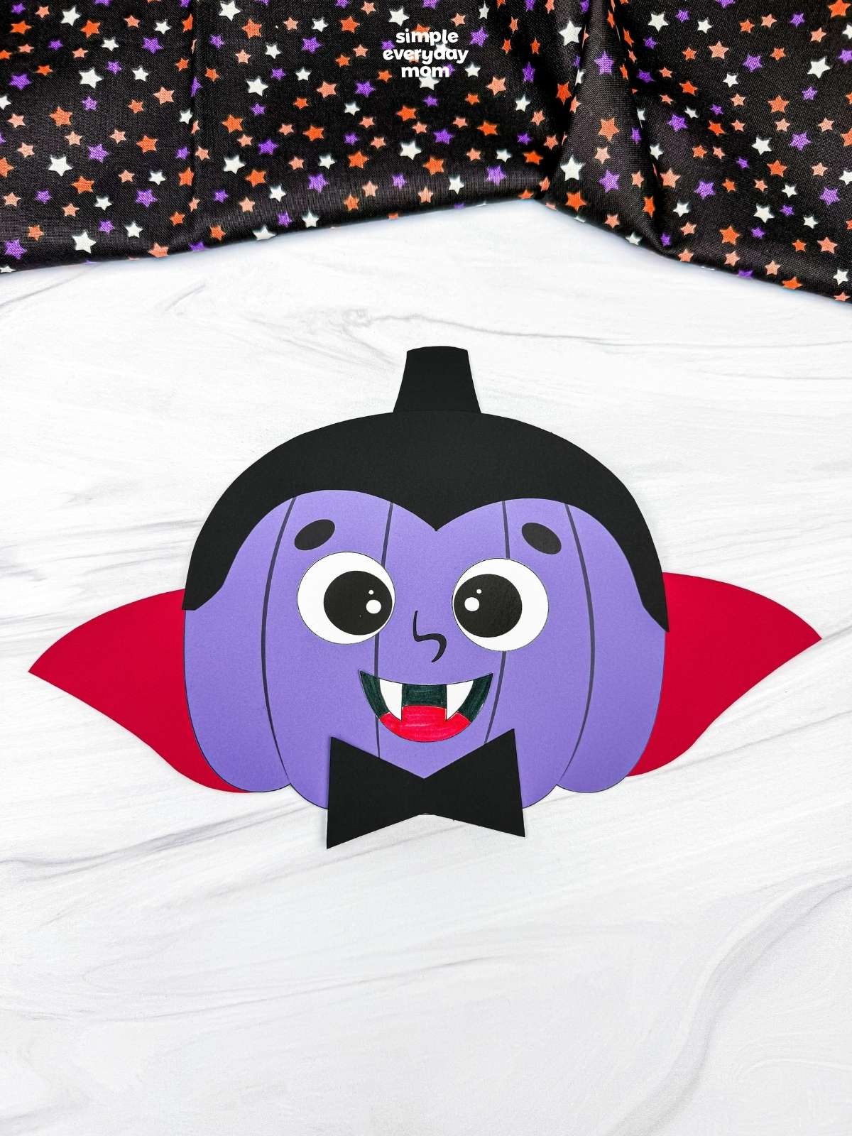 A completed craft showing a vampire pumpkin disguise with a cape, fangs, bow tie, and black hair.