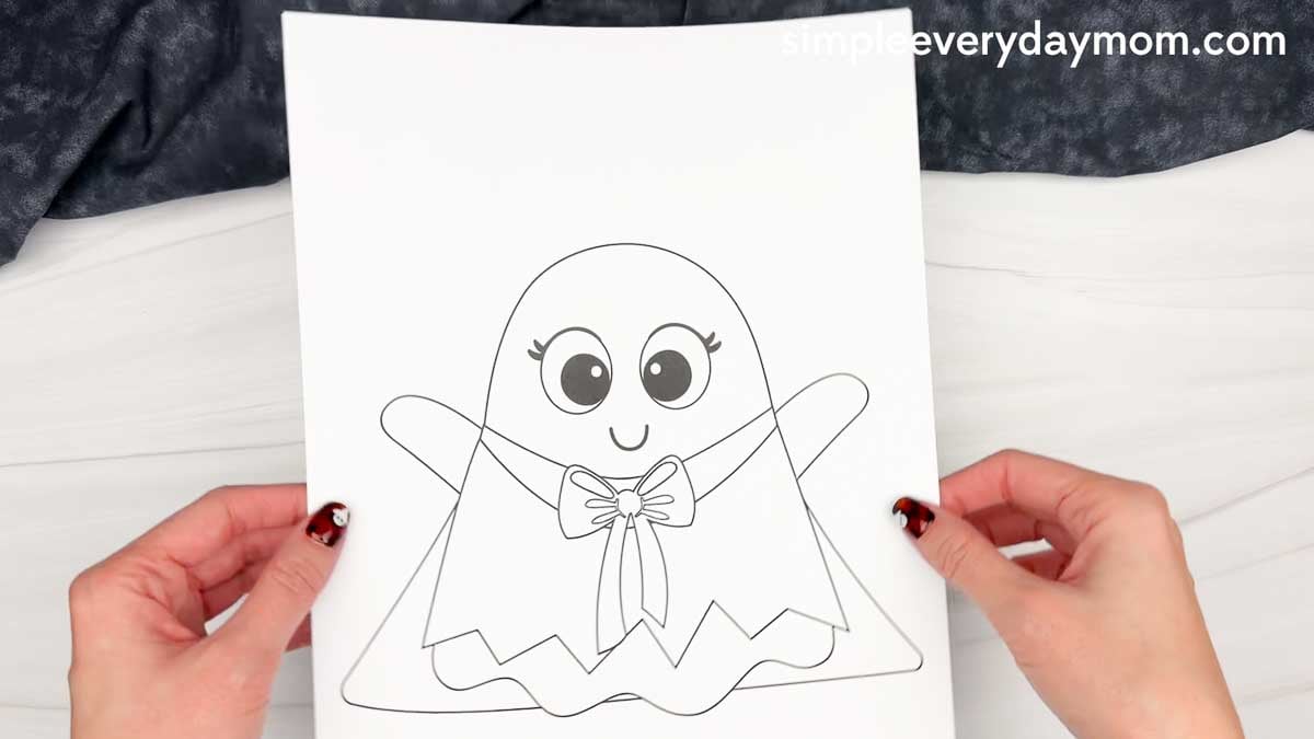 Hands holding a printable ghost template with a bow for a Witch Ghost Disguise craft.