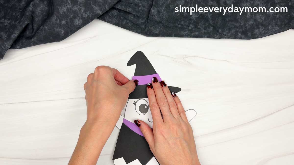 Hands attaching the hat band across the witch hat on the ghost disguise craft.