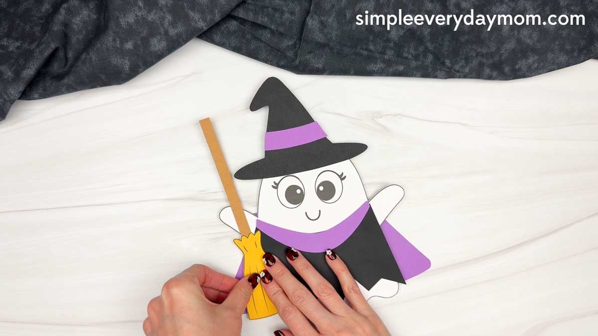 Hands attaching the finished broom to the side of the Witch Ghost Disguise craft.