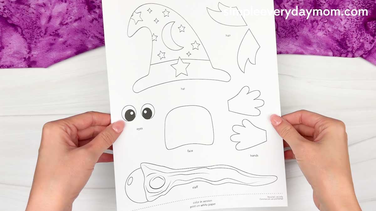 Hands holding a printed Wizard Handprint Craft template featuring the hat, hair, eyes, face, hands, and staff pieces.