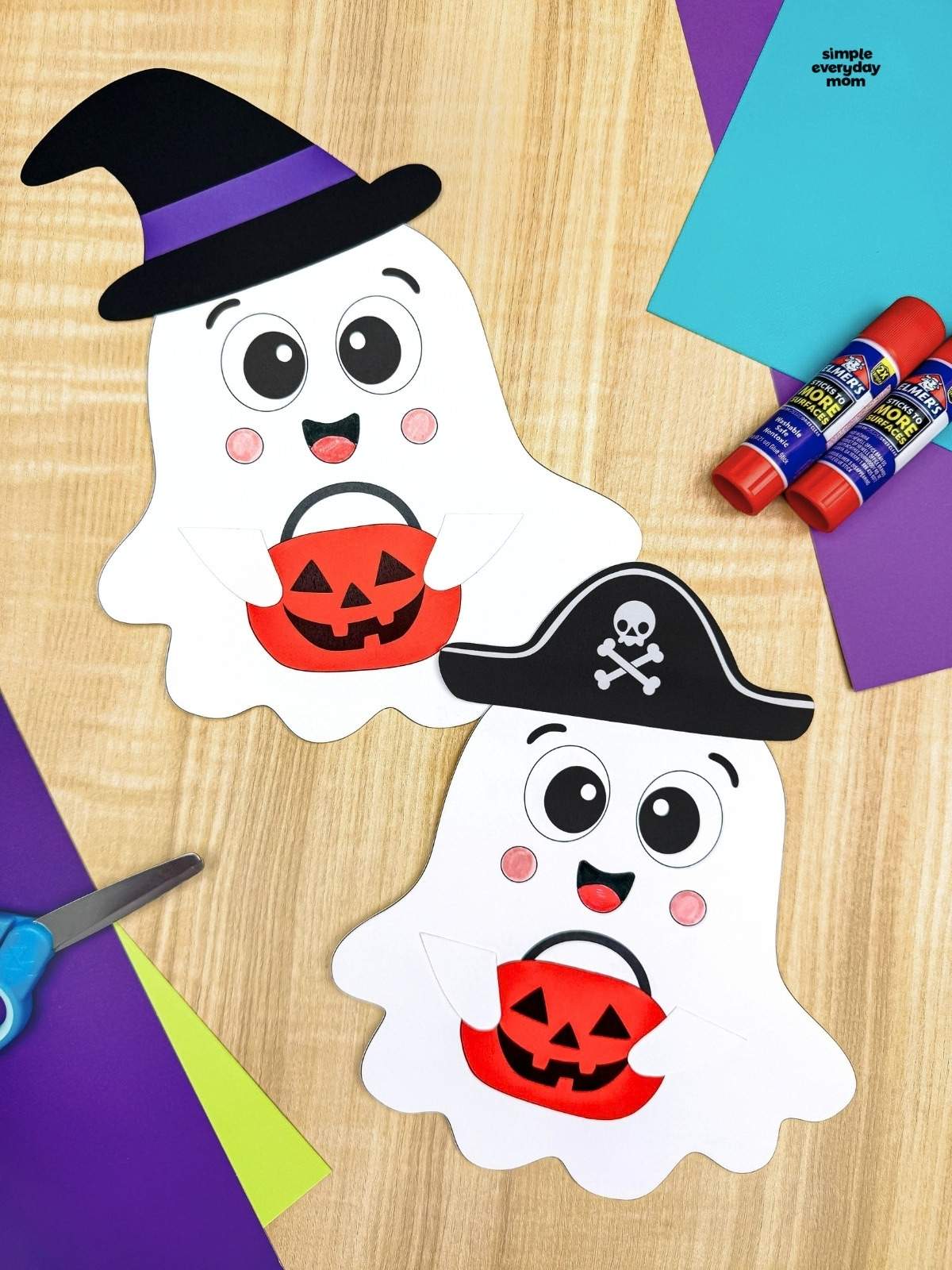 A completed craft pair of smiling Halloween paper ghosts wearing witch and pirate hats and holding orange pumpkin buckets.