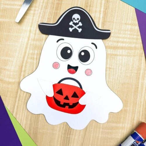 A completed craft featuring a smiling Halloween paper ghost wearing a pirate hat and holding an orange pumpkin bucket.