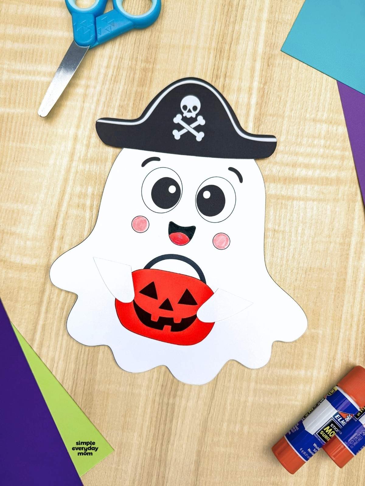 A completed craft featuring a smiling Halloween paper ghost wearing a pirate hat and holding an orange pumpkin bucket.