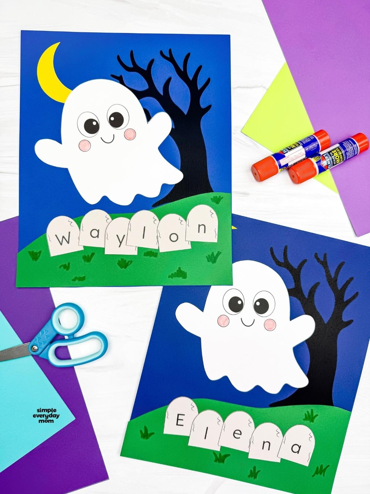 A completed Craft showing two Halloween Ghost Name Crafts with smiling ghosts, crescent moons, spooky trees, and personalized letter tombstones surrounded by colorful paper and craft supplies.