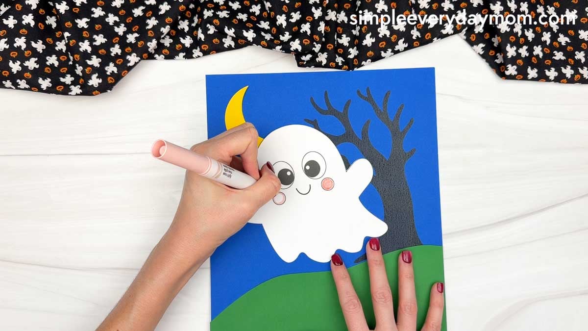 Hands coloring the ghost's cheeks pink with a marker for the Halloween Ghost Name Craft.