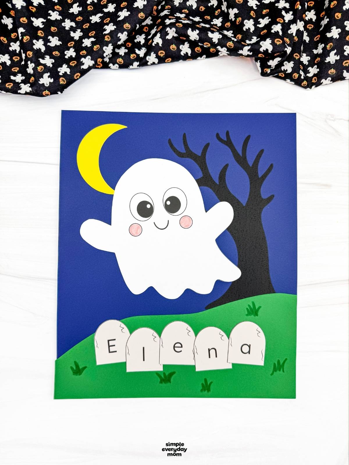 A completed Craft featuring a smiling ghost, crescent moon, spooky tree, and tombstones spelling a child's name for a fun Halloween name recognition activity.
