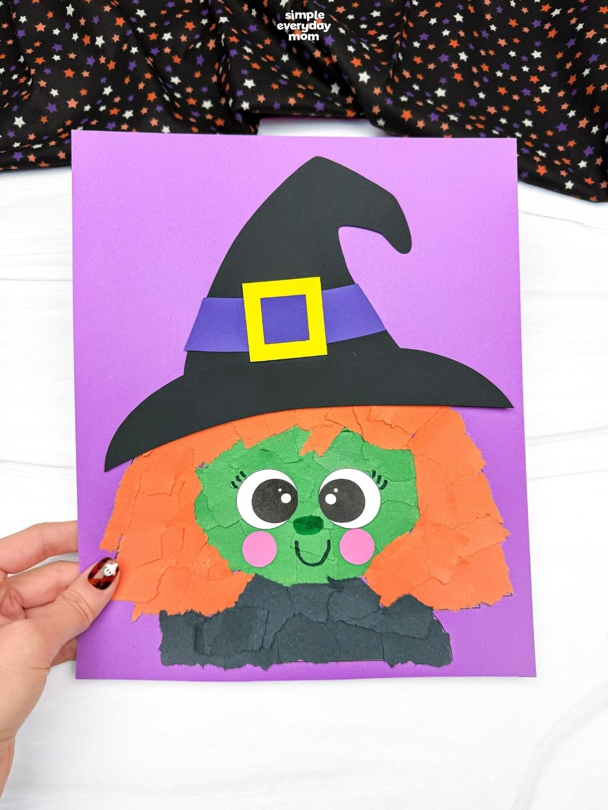 Hands holding a completed Witch Torn Paper Craft featuring orange torn paper hair, a green face, and a black witch hat on a purple background.
