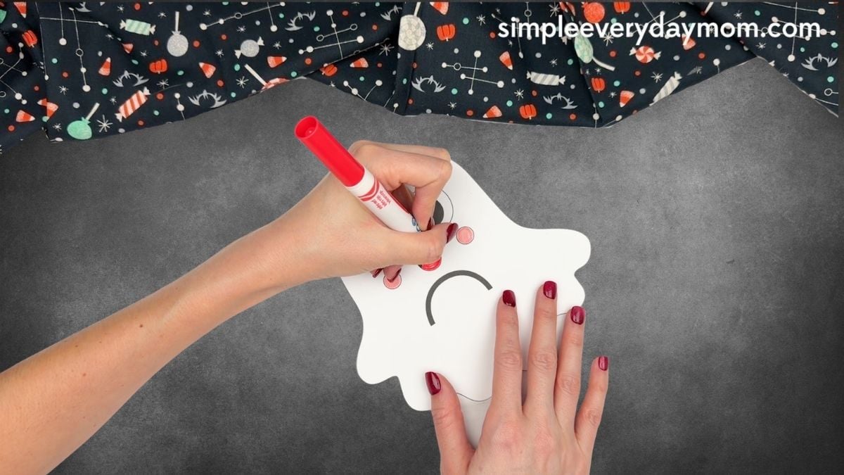 Hands coloring the tongue red on a Halloween paper ghost craft with a marker.